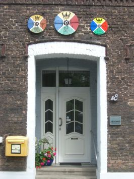 Hünxe-Krudenburg : Die hölzernen Scheiben des Schützenvereins an der Hauswand zeigen den Namen, das Jahr, des Schützenkönigs und einen Frosch im Wappen. Im Ort gibt es noch mehr von diesen Scheiben zu sehen.